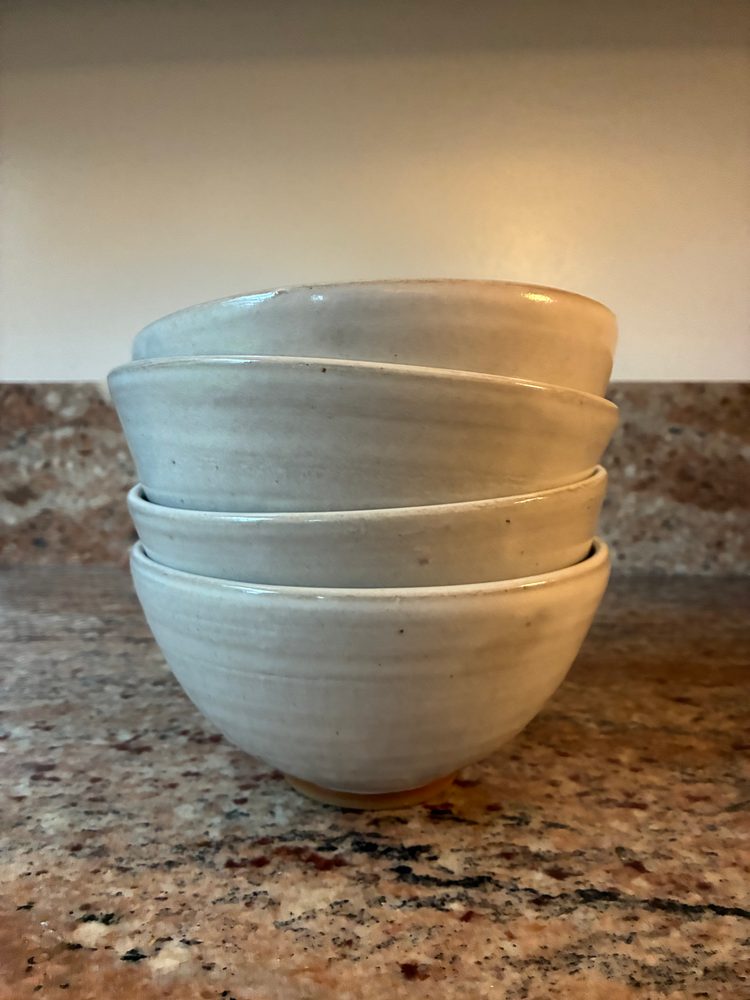 The set of 4 bowls, white glaze on brown clay, stacked on a granite counter