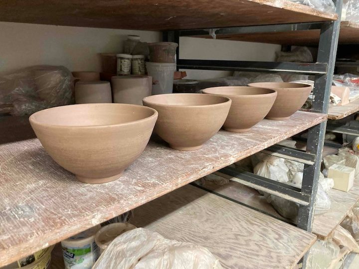 The 4 bowls before glazing, bare brown clay, in a row on a studio shelf