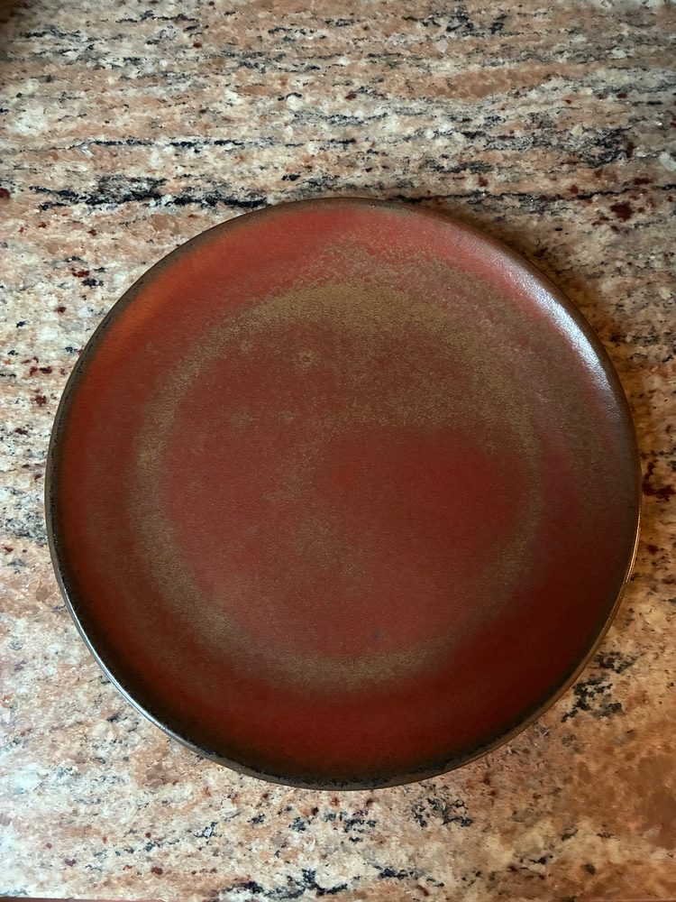 One plate from the set seen from above, its red glaze breaking to a golden-brown ring
